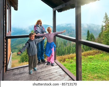 Family On Wooden Cottage Porch On Mountain Hill Top And Sunshine