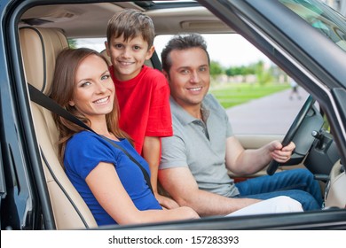 Family With One Kid Is Travelling By Car, Smiling And Looking At Camera