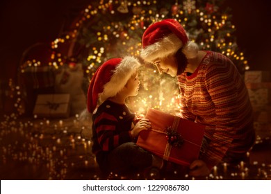 Family Open Christmas Lighting Present Gift Box Front Of Xmas Tree, Happy Mother With Baby Child In Magic Night