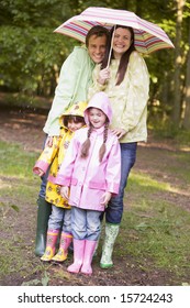 Family Outdoors In Rain With Umbrella Smiling