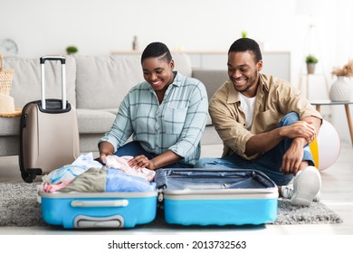 Family Packing Suitcase For Vacation. Happy Black Spouses Sitting Near Suitcase Preparing For Travel Together In Living Room At Home. African American Tourists Posing With Luggage Concept - Powered by Shutterstock