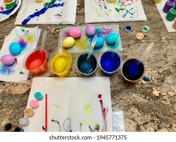 A Family Painting Easter Eggs With Paint, Cups Of Dye, Paper Towels, Paint Brushes, And Creative Space. The Dyed Eggs Are Colorful And A Blank Canvas To Show Some Artistic Creativity. A Colorful Mess!