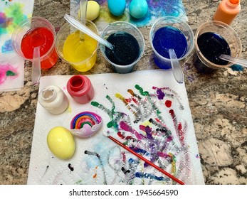 A Family Painting Easter Eggs With Wet Paint. Dyed Eggs With A Rainbow Painted On, Colorful Paint Streaks, Dye Cups, Paint Brushes, And Paper Towels. It's A Creative Outlet And A Big, Colorful Mess.