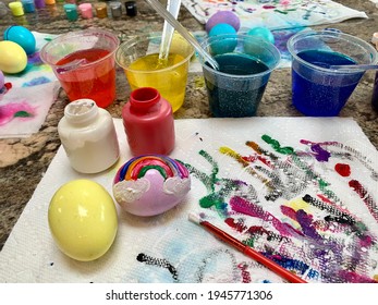 A Family Painting Easter Eggs With Wet Paint. Dyed Eggs With A Rainbow Painted On, Colorful Paint Streaks, Dye Cups, Paint Brushes, And Paper Towels. It's A Creative Outlet And A Big, Colorful Mess.