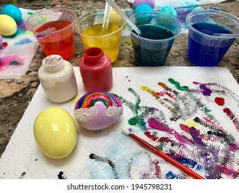 A Family Painting Easter Eggs With Wet Paint. Dyed Eggs With A Rainbow Painted On, Colorful Paint Streaks, Dye Cups, Paint Brushes, And Paper Towels. It's A Creative Outlet And A Big, Colorful Mess.