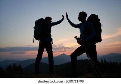 Family pair of hikers fun clapping each other's hands when they reached top of the mountain during outdoor hike. Evening hiking on mountain hills in twilight under evening sky. Concept of travelling.
