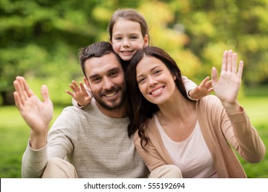 family, parenthood, adoption and people concept - happy mother, father and little girl in summer park waving hands