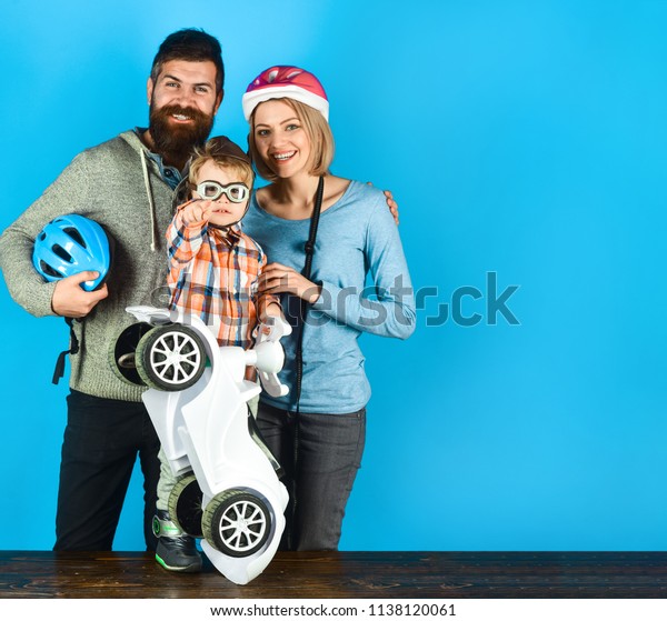 Family. Parenthood. Adoption and people concept.
Happy mother and father in protective helmet. Boy holds toy car in
hands. Boy in helmet and glasses holds driving toy car. Vacation
and leisure.