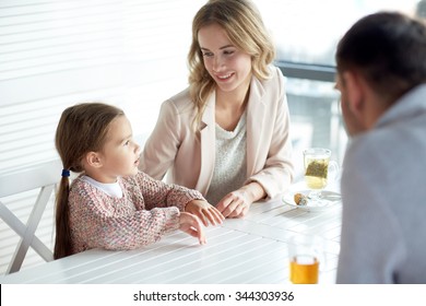 Family, Parenthood, Communication And People Concept - Happy Mother, Father And Little Girl Having Dinner And Talking At Restaurant Or Cafe