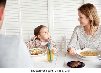 Family, Parenthood, Communication And People Concept - Happy Mother, Father And Little Girl Having Dinner And Talking At Restaurant Or Cafe