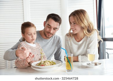 Family, Parenthood, Food And People Concept - Happy Mother, Father And Little Girl Eating Pasta For Dinner At Restaurant Or Cafe