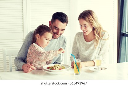 Family, Parenthood, Food And People Concept - Happy Mother, Father And Little Girl Eating Pasta For Dinner At Restaurant Or Cafe