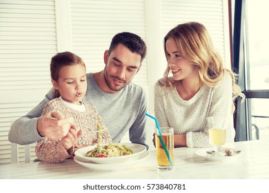 Family, Parenthood, Food And People Concept - Happy Mother, Father And Little Girl Eating Pasta For Dinner At Restaurant Or Cafe