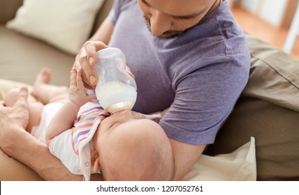 family, parenthood and people concept - close up of father feeding little daughter with baby formula from bottle at home - Powered by Shutterstock