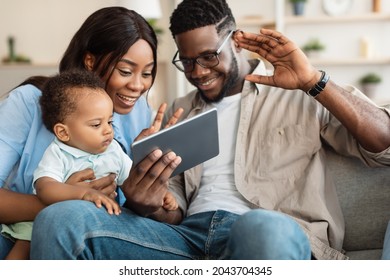 Family, Parenthood And Technology Concept. Portrait Of Happy Smiling Black Parents Holding Little Baby On Hands Having Video Call On Tablet Computer At Home, Waving To Screen, Talking With Relatives