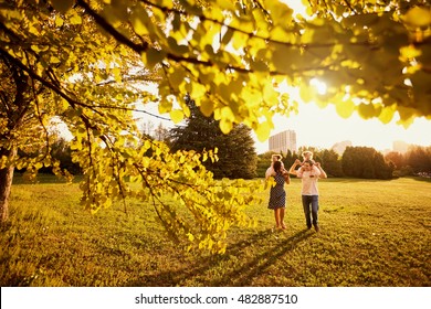 The Family In The Park. Happy Parents With Children Walk In The Nature In The Evening At Sunset.