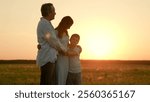 Family in park, kids hugging parents in sun rays on field. Mother dad son daughter. Family, kids weekend in nature. Kids mom dad hugging on lawn. Family hugs at sunset dad mom daughter son, silhouette