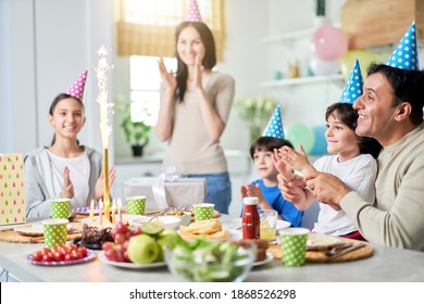 Family Party. Happy Latin American Family With Children Looking Suprised About Firework Sparkler On A Cake While Celebrating Birthday Together At Home