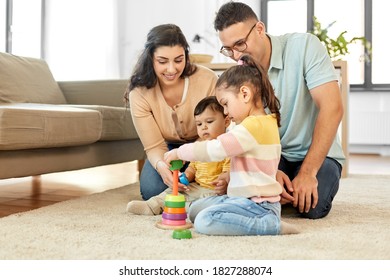 family and people concept - happy mother, father, little daughter and baby son playing with pyramid toy at home - Powered by Shutterstock