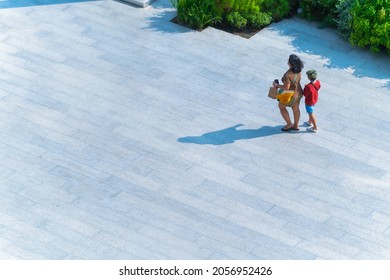 Family People Walking In The Street. Back Of Woman And Kid Walk Across On Concrete Pavement In Sunny Day. Summer Season Of Crowd Life. (wide Angle Of Aerial Top View)