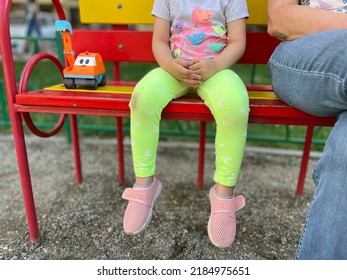 A family photo of a little girl, her grandmother and a favorite bright toy truck (excavator) having a rest on the vivid bench in a park. People relax on the bench on a playground - Shutterstock ID 2184975651