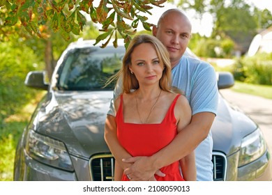 Family Photo Session Of An Adult Husband And Wife In Front Of Their Car.