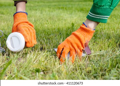 Family Picking Up Trash In Spring Park Wearing Protective Gloves, Focus On Boy Hand With Plastic Glass