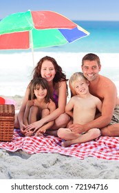 Family Picnicking Under A Sol Umbrella On The Beach