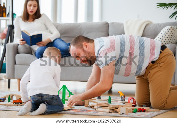 Family picture of father and son playing on floor in\
toy road with cars