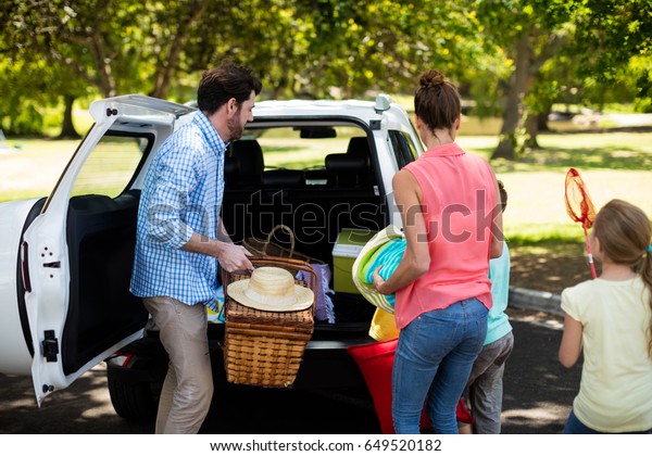 Family placing\
picnic items in car trunk at\
park