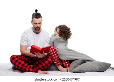 Family In Plaid Sleepwears On White Studio. Dad Reading Bedtime Story сurly Short-haired Daughter In Red Pajama. Female Child Sit Wrapped In Blanket On Bed And Looks Her Father. Leisure Time