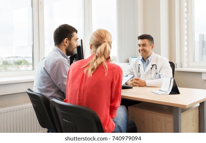 Family Planning, Medicine, Fertility And Healthcare Concept - Couple Visiting Doctor And Filling Form At Clinic