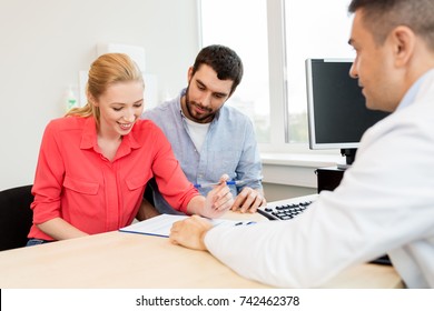 Family Planning, Medicine, Fertility And Healthcare Concept - Couple Visiting Doctor And Filling Form At Clinic