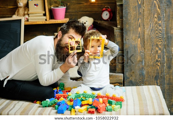 Family play with constructor at home. Dad and\
child play with details of constructor, looking through. Nursery\
with chalkboard on background. Father and son play with\
constructor. Fatherhood\
concept.