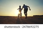 family play in the park. father teaching daughter to ride a bike. happy family kid dream concept. daughter learn to ride bike silhouette. father supporting child riding sunset bike summer in park