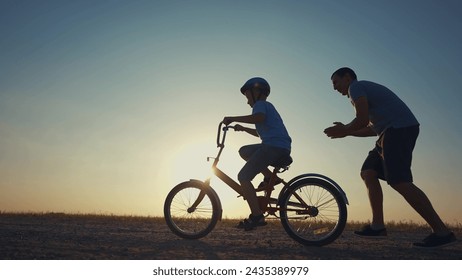 family play in the park. father teaching son to ride a bike. happy family kid dream concept. son learn to ride bike silhouette. father supporting sunset child son riding bike summer in the park - Powered by Shutterstock