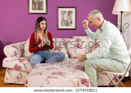 A  family is playing a board game. A father and his teenage daughter are having a great time playing cards in the living room.