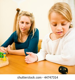 Family Playing A Board Game At Home, Daughter Is Rolling The Dice And Looks Disappointed At The Outcome