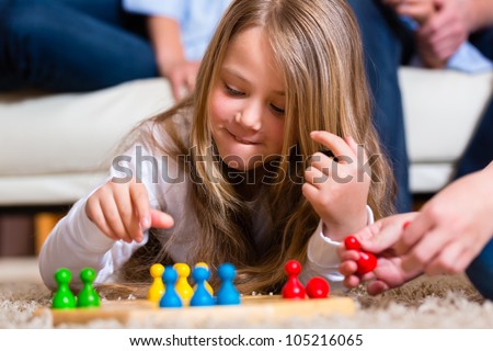 Family playing board game ludo at home on the floor, close up on child