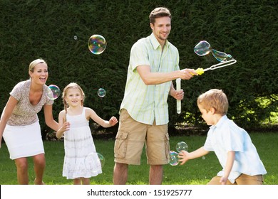 Family Playing With Bubbles In Garden