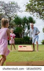 Family playing cornhole game by the sea on sunny summer day. Parents and children playing bean bag toss