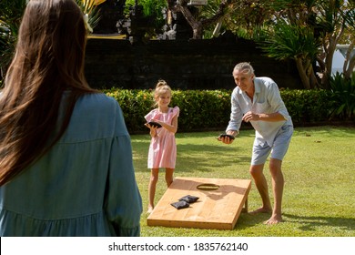 Family playing cornhole game outdoor on sunny summer day. Parents and children playing bean bag toss