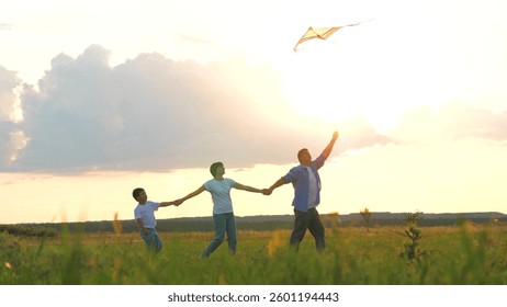 Family playing with flying kite holding hands at sunset grass wheat field outdoor leisure. Happy mother father and son relaxing enjoy freedom lifestyle weekend activity at meadow nature landscape