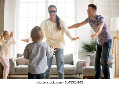 Family playing hide and seek game together with blindfolded mother, happy kids and parents having fun in living room, children hiding clapping hands enjoying interesting activity with mom dad at home