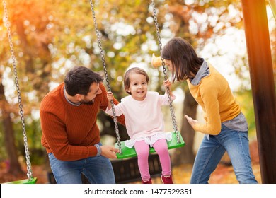 Family playing at a park together, having fun. The children, a 3 year old girl are on a swing set and their parents are pushing her swings. - Powered by Shutterstock