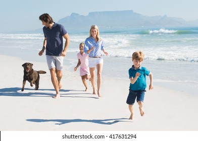 Family playing with pet on the beach. Happy beautiful family running at beach with pet dog. Smiling parents with son and daughter having fun at seaside.
