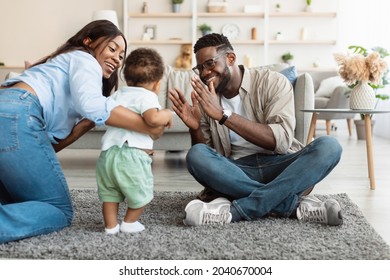 Family Playing Together. Adorable Cute Baby Boy Learning How To Walk, Happy Mom Proud Of Little Child Helping And Teaching Him Sitting On Floor Carpet, Dad Clapping Hands. First Steps.