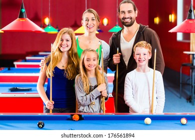 Family Playing Together Billiard With Queue And Balls On Pool Table 