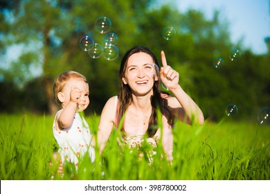 Family Playing Together Outside. Mom And Little Daughter Cheerfully Catching Soap Bubbles. Portrait Of Happy Joyful Family Of Mum And Child.