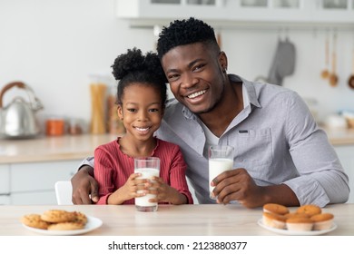 Family Portrait Of Black Father And Daughter Bonding While Having Healthy Breakfast Together At Kitchen, Sitting At Table, Eating Homemade Pastry, Drinking Fresh Milk, Cheerfully Smiling At Camera